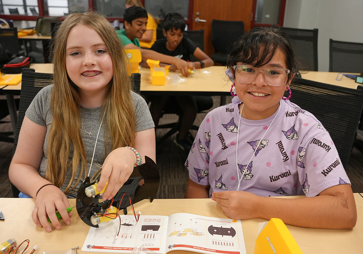 Two young girls working with tools in a classroom setting.